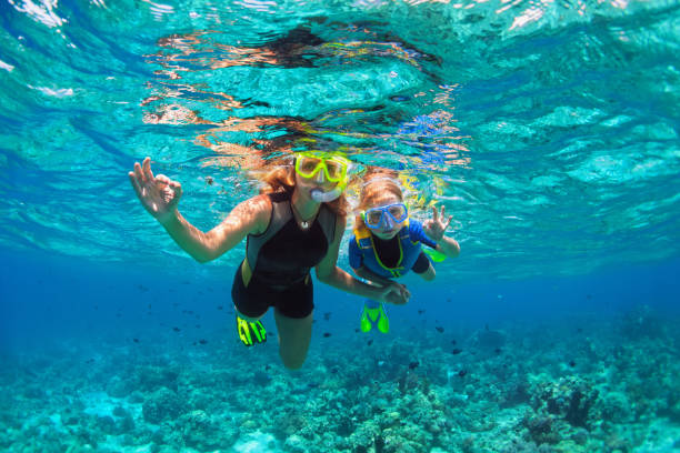 Happy family - mother, kid in snorkeling mask dive underwater with tropical fishes in coral reef sea pool. Show by hands divers sign OK. Travel lifestyle, beach adventure on summer holiday with child.